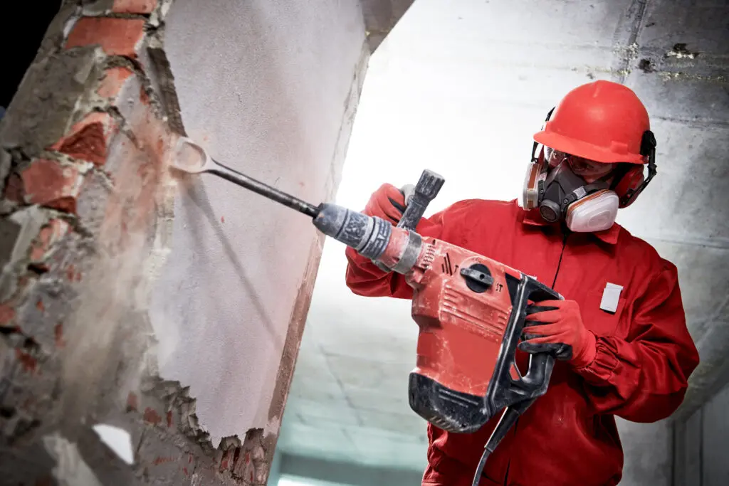 Man taking down wall of old building with machine.