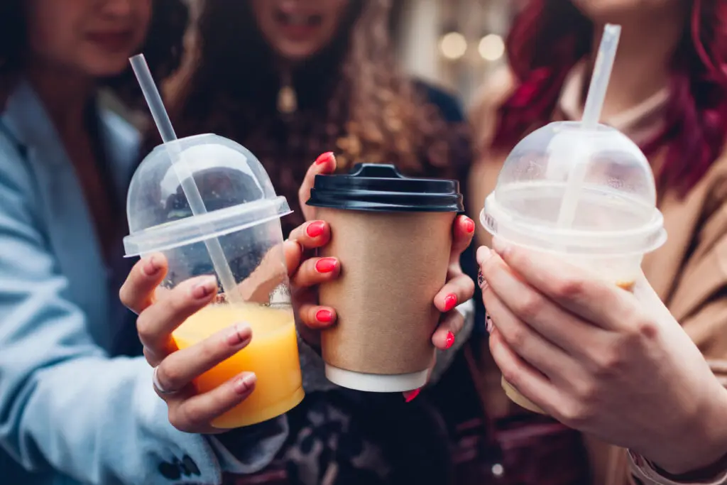 Friends holding drinks in a plastic cup and coffee cup.